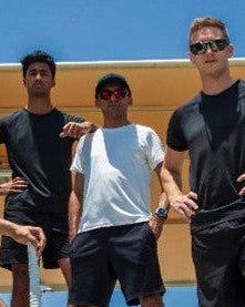 Five men showcasing Qwicket apparel on steps outside a Dubai stadium with a clear blue sky.