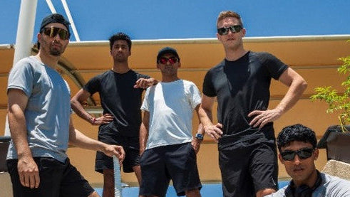 Five men showcasing Qwicket apparel on steps outside a Dubai stadium with a clear blue sky.